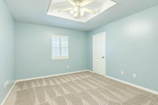 carpeted spare room featuring a tray ceiling, baseboards, and ceiling fan