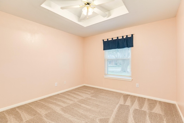spare room featuring light carpet, a ceiling fan, baseboards, and a raised ceiling