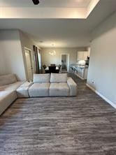 living room with a raised ceiling, ceiling fan, and dark hardwood / wood-style floors