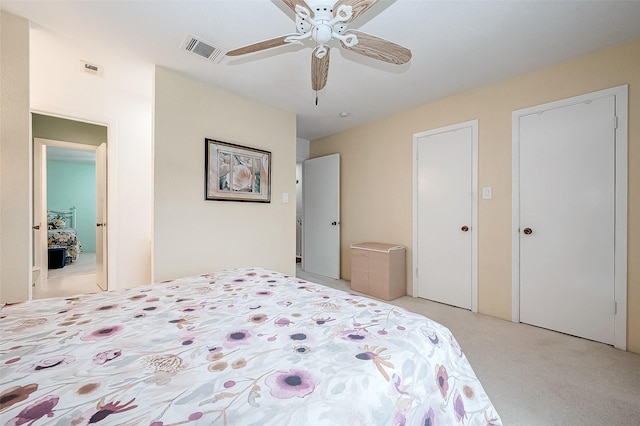 bedroom featuring ceiling fan, light colored carpet, and two closets