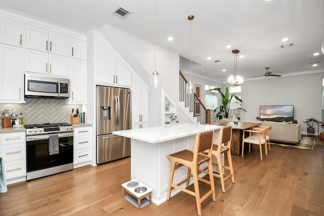 kitchen featuring stainless steel appliances, white cabinets, decorative backsplash, and hanging light fixtures