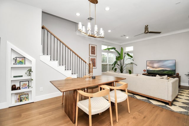 dining room with ceiling fan with notable chandelier, built in shelves, light wood-type flooring, and crown molding