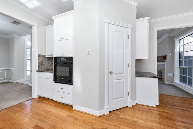 kitchen with black oven, white cabinetry, ornamental molding, and a textured ceiling