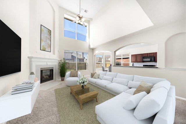 living room featuring a tiled fireplace, ceiling fan, and a high ceiling