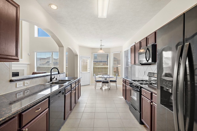 kitchen featuring decorative light fixtures, light tile patterned floors, black appliances, dark stone counters, and sink