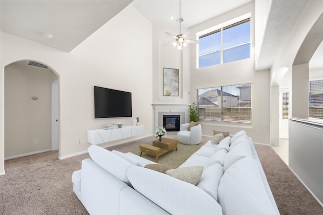 living room with a towering ceiling, a tile fireplace, light colored carpet, and ceiling fan