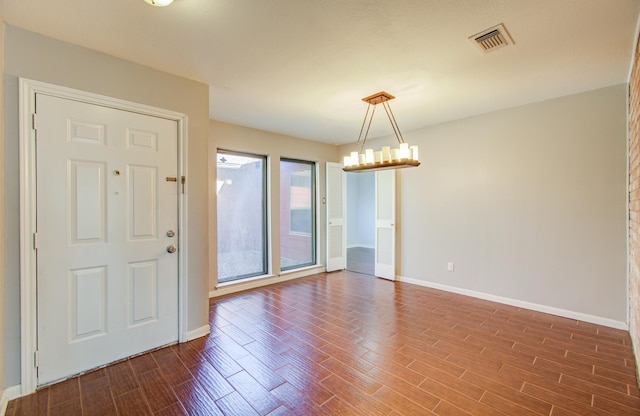 spare room featuring baseboards, dark wood-style flooring, a chandelier, and visible vents
