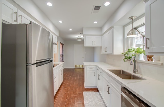 kitchen featuring appliances with stainless steel finishes, pendant lighting, white cabinetry, sink, and light stone countertops