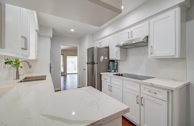 kitchen featuring black electric cooktop, sink, stainless steel refrigerator, and white cabinets