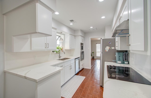 kitchen with appliances with stainless steel finishes, range hood, white cabinetry, sink, and light stone countertops