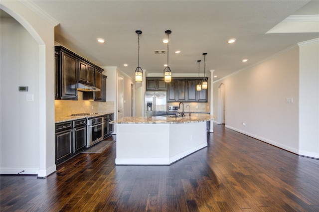 kitchen featuring pendant lighting, dark brown cabinets, stainless steel appliances, a center island with sink, and decorative backsplash