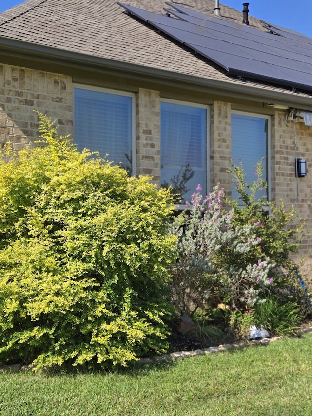view of home's exterior featuring brick siding, roof with shingles, and solar panels