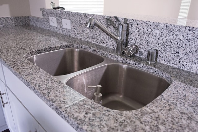 room details with sink, white cabinets, tasteful backsplash, and light stone counters