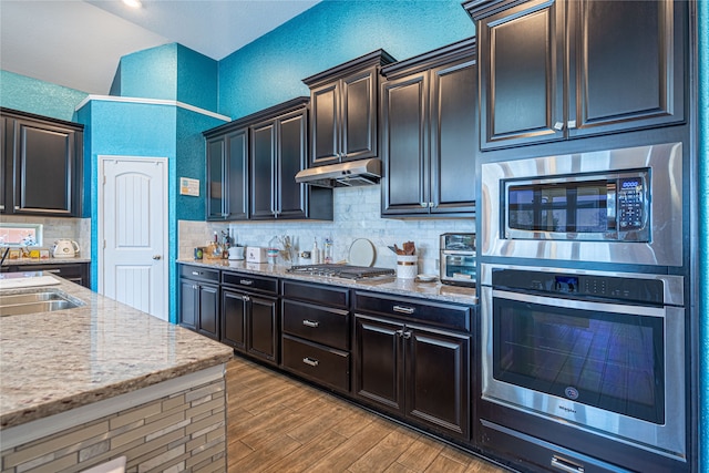 kitchen with tasteful backsplash, sink, hardwood / wood-style flooring, stainless steel appliances, and light stone counters