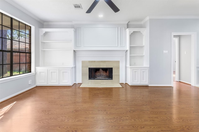 unfurnished living room featuring a tile fireplace, built in features, ceiling fan, and hardwood / wood-style floors