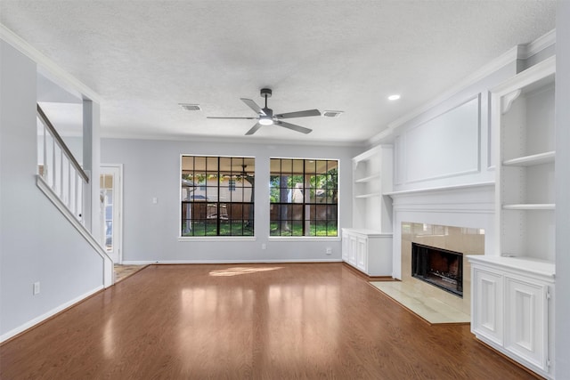 unfurnished living room featuring wood-type flooring, a tiled fireplace, crown molding, a textured ceiling, and built in shelves