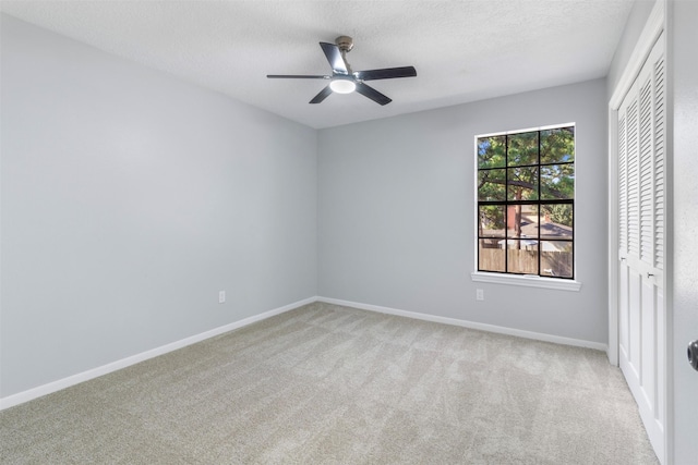 empty room featuring a textured ceiling, light carpet, and ceiling fan