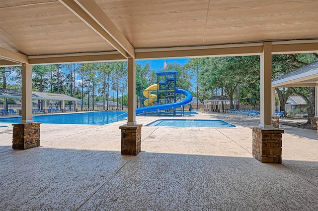 view of swimming pool with a water slide, a patio area, and a playground