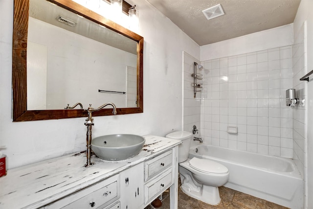 full bathroom with toilet, a textured ceiling, tiled shower / bath, and vanity