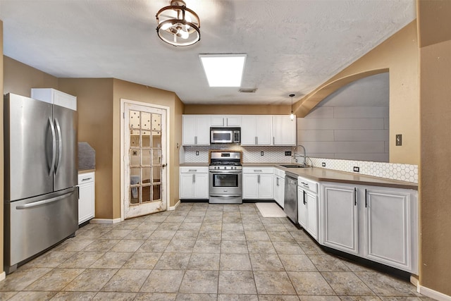 kitchen with appliances with stainless steel finishes, pendant lighting, decorative backsplash, sink, and white cabinetry