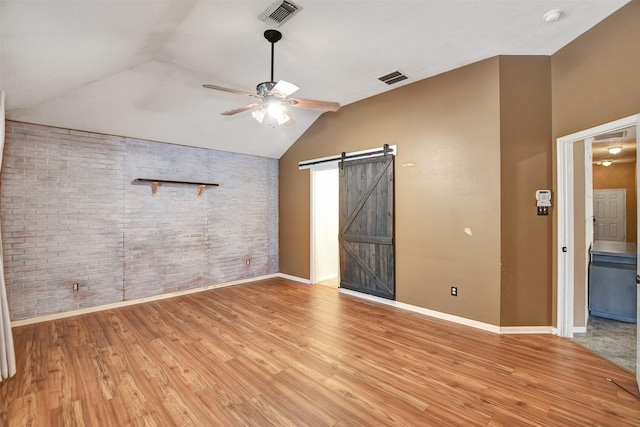 unfurnished bedroom featuring lofted ceiling, ceiling fan, light hardwood / wood-style flooring, a barn door, and brick wall