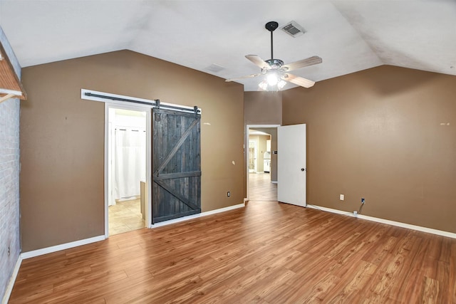 unfurnished bedroom featuring lofted ceiling, ceiling fan, light hardwood / wood-style floors, and a barn door