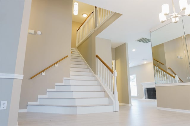 staircase with a high ceiling, a tile fireplace, a notable chandelier, and hardwood / wood-style floors