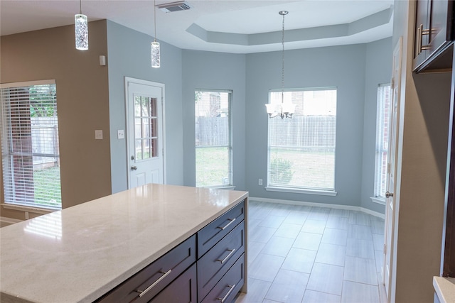 kitchen with light stone countertops, a chandelier, hanging light fixtures, a raised ceiling, and a kitchen island