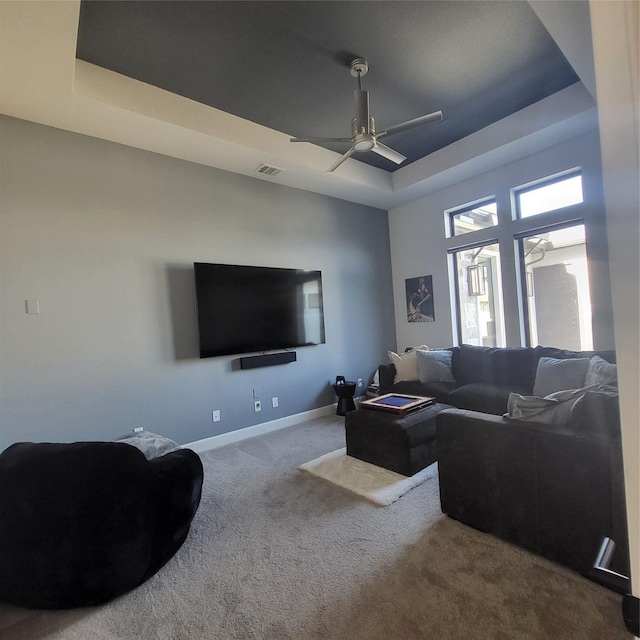 carpeted living room with ceiling fan and a raised ceiling