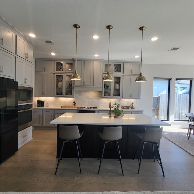 kitchen featuring light wood-type flooring, a kitchen island with sink, gray cabinets, and oven