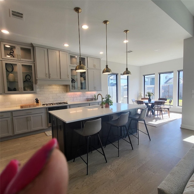 kitchen with a kitchen bar, gray cabinetry, a kitchen island with sink, light wood-type flooring, and hanging light fixtures