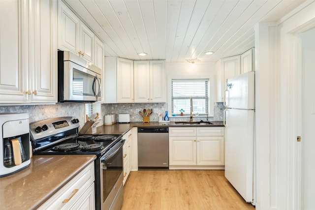 kitchen with dark countertops, light wood finished floors, decorative backsplash, appliances with stainless steel finishes, and a sink