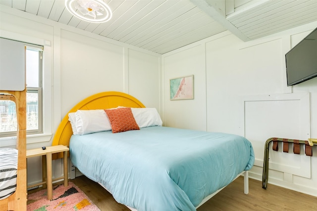 bedroom with wood ceiling, a decorative wall, and wood finished floors