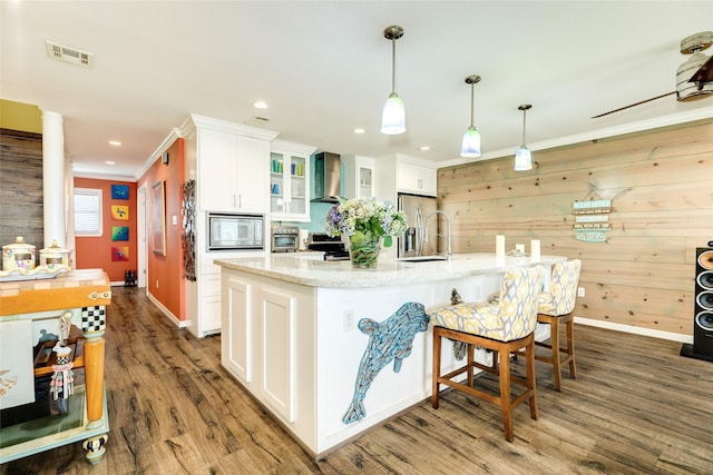 kitchen featuring white cabinets, a kitchen island with sink, stainless steel appliances, sink, and wall chimney range hood