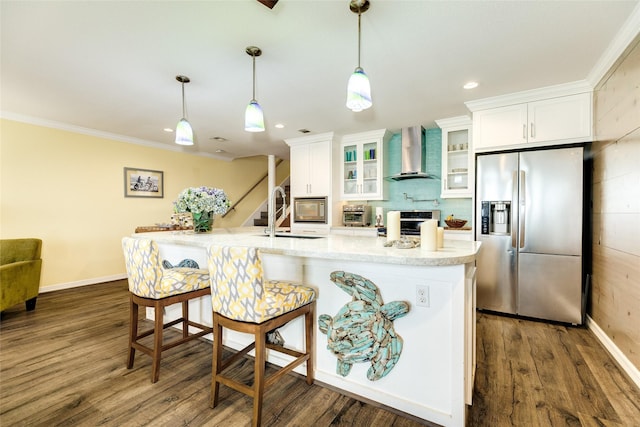 kitchen featuring stainless steel appliances, sink, white cabinetry, hanging light fixtures, and wall chimney range hood