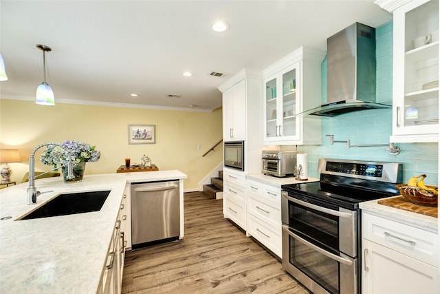 kitchen featuring stainless steel appliances, sink, white cabinetry, hanging light fixtures, and wall chimney range hood