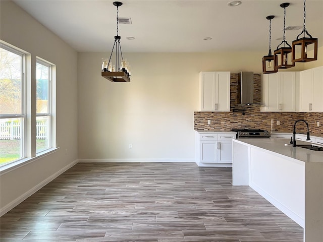 kitchen featuring sink, white cabinets, wall chimney exhaust hood, a wealth of natural light, and hanging light fixtures