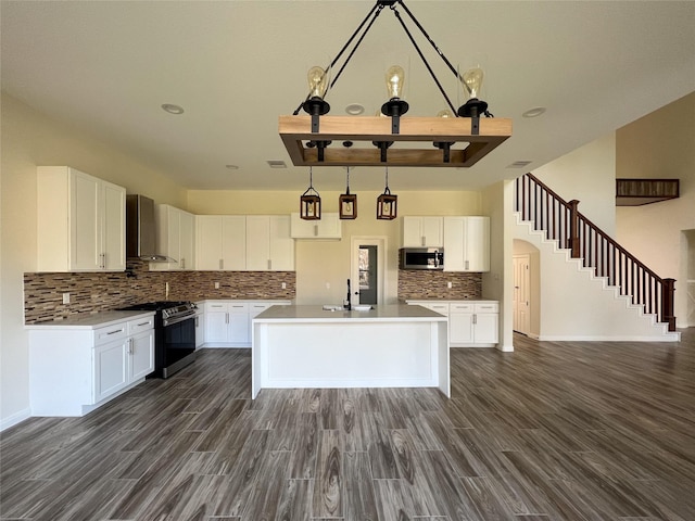 kitchen featuring stainless steel appliances, a kitchen island, wall chimney range hood, and white cabinetry