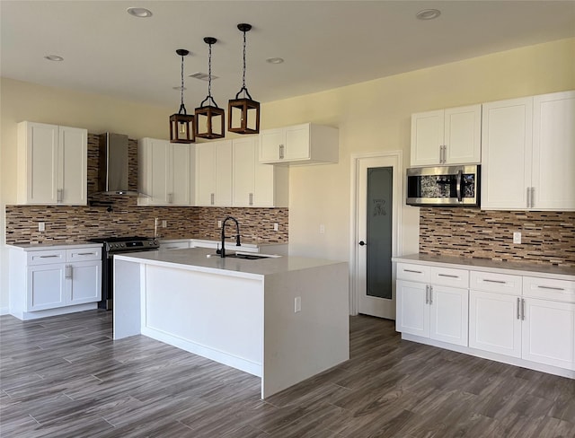 kitchen with wall chimney exhaust hood, pendant lighting, stainless steel appliances, a kitchen island with sink, and white cabinetry