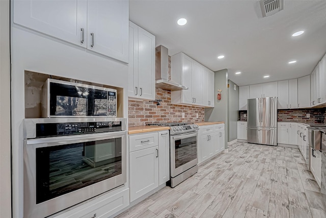 kitchen featuring appliances with stainless steel finishes, wall chimney exhaust hood, backsplash, and white cabinetry