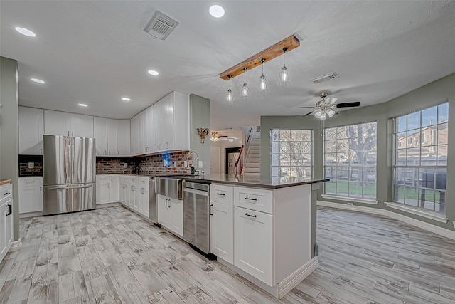 kitchen with decorative light fixtures, white cabinets, kitchen peninsula, backsplash, and appliances with stainless steel finishes