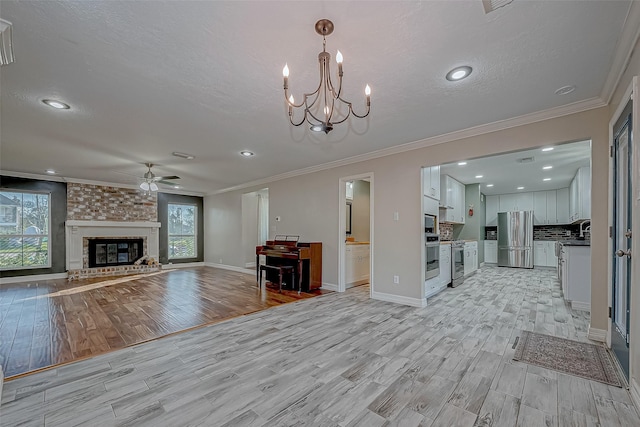 unfurnished living room with ceiling fan with notable chandelier, a brick fireplace, a textured ceiling, and crown molding