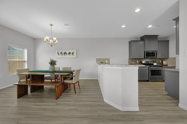 kitchen featuring gray cabinets, appliances with stainless steel finishes, a notable chandelier, pendant lighting, and tasteful backsplash