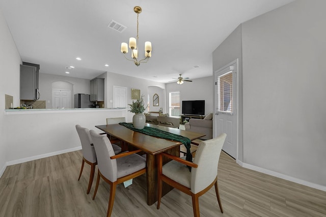 dining space with ceiling fan with notable chandelier and light hardwood / wood-style floors