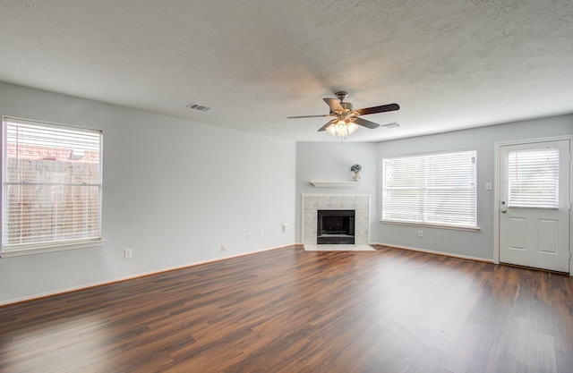 unfurnished living room featuring ceiling fan, plenty of natural light, a tile fireplace, and dark hardwood / wood-style flooring