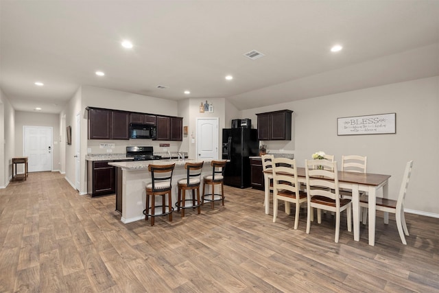 kitchen with a center island with sink, dark brown cabinetry, black appliances, and light hardwood / wood-style flooring