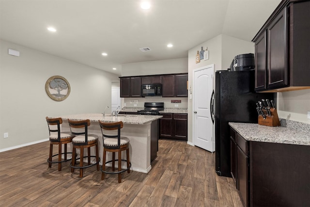 kitchen with black appliances, an island with sink, light stone countertops, dark hardwood / wood-style flooring, and sink