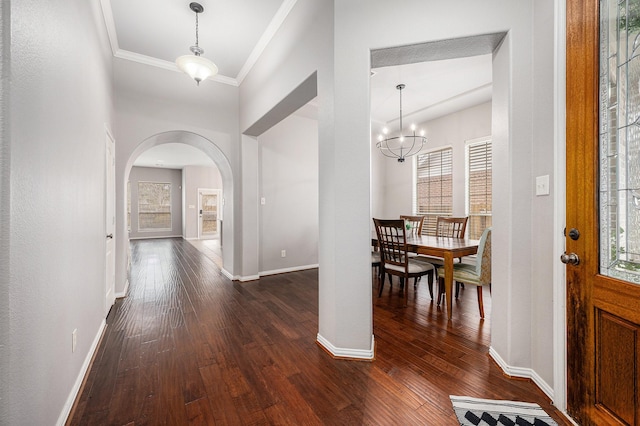 foyer entrance featuring dark wood-style floors, arched walkways, a notable chandelier, crown molding, and baseboards