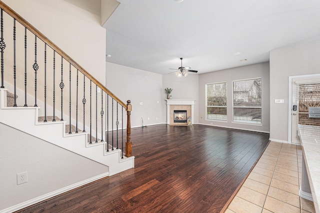 unfurnished living room featuring ceiling fan, wood finished floors, baseboards, stairway, and a glass covered fireplace