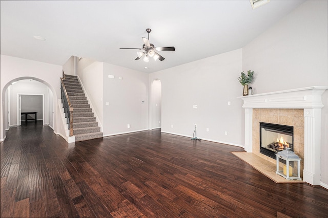 unfurnished living room featuring arched walkways, ceiling fan, a fireplace, wood finished floors, and stairway